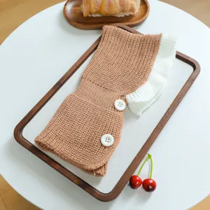 Detail view of brown knitted pet hat with white frilly edge and buttons for small dogs.