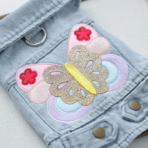 Close-up detail of pet denim clothes showing colorful butterfly embroidery, buttons, and D-ring.