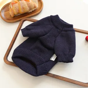 Detailed close-up view of the dark blue knitted pet sweater with brand tag on a wooden tray.