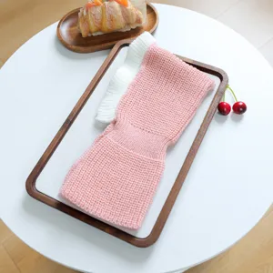 Close-up detail shot of the cute pink and white knitted pet hat with frilly edge on wooden tray.