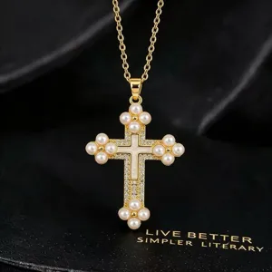 Detailopname van de gouden kruishanger met sprankelende zirkoon en elegante parelaccenten.