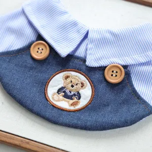 Dettaglio in primo piano della bavetta per animali con jeans, colletto a righe e ricamo.