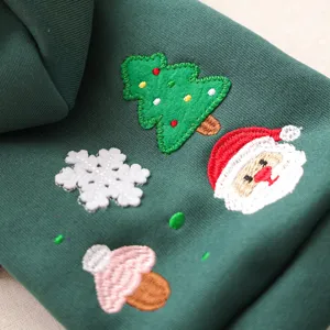 Close-up van groene huisdierhoodie met schattige geborduurde kerstboom en kerstmanpatronen erop.