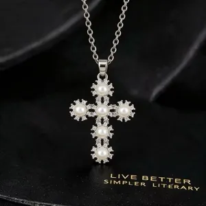 Close-up van een zilveren kruisketting met delicate parels en sprankelende zirkoniasteentjes.