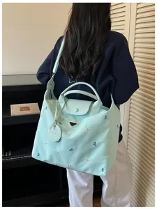 Detailed view of the light blue shoulder bag featuring embroidered bows and a triangle logo.