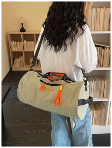 Detail view of a large capacity khaki cylindrical gym duffel bag with orange strap accents.
