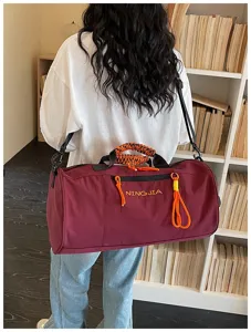 Large capacity cylindrical gym duffel bag in maroon with orange woven accents for travel.