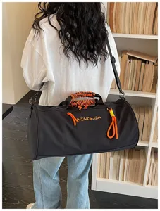 Detailed view of the black cylindrical travel sports duffel bag with orange braided handle accents.