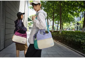 Outdoor lifestyle detail view of a stylish color-blocked canvas shoulder and travel tote bag.