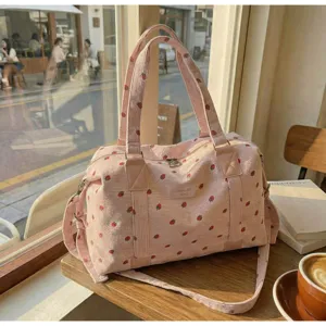 Detailed shot of the pink corduroy travel duffel bag with cute strawberry print on a cafe table.