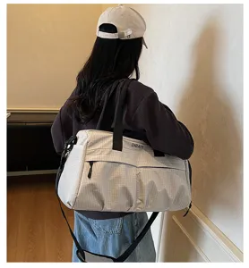 Vue détaillée du grand sac de voyage à motif quadrillé porté sur l'épaule par le modèle.