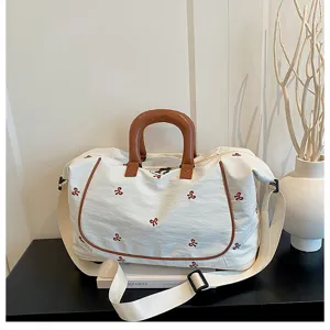 Canvas travel duffel bag with stylish brown leather handles and charming bow embroidery details.