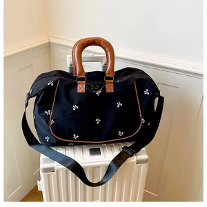 Detailed view of black travel duffel bag with white bows and brown leather handles on luggage.