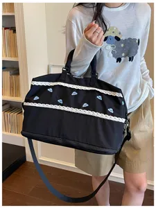 Detail view of the black travel duffel bag featuring white lace trim and blue cloud embroidery.