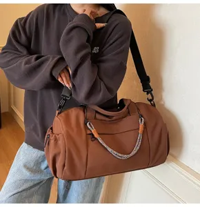Detalle de bolsa de viaje marrón con asa tejida, bolsillo lateral y correa ajustable.