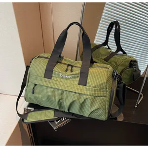 Détail de sac de voyage à carreaux verts, montrant la texture du tissu, les zips et les crochets.