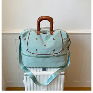 Travel duffel bag detail showing mint green canvas, brown leather handles, and cute bows.