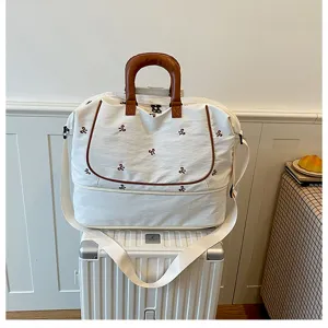 White canvas travel duffel bag with brown handles and cute embroidered bows for short trips.