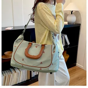 Close-up detail of light green travel duffel bag with ribbon embroidery and brown handles.