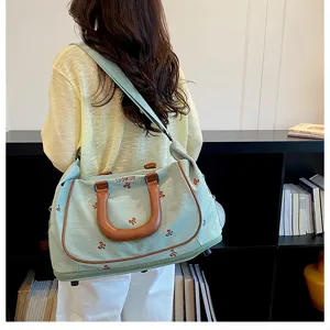Detailed view of light green travel duffel bag with bow embroidery and brown handles.