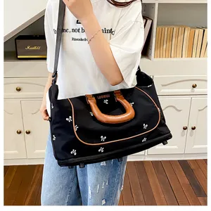 Detail shot of black travel duffel bag with bow prints and brown handles carried by model.