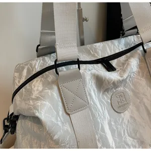 Close-up detail of silver crinkled travel duffel gym bag with wide strap and logo patch.