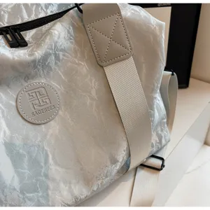 Close-up of silver crinkled PU travel gym bag with wide strap and SAGEREES logo patch.