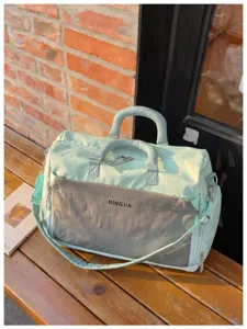 Close-up detail of the light green travel duffel bag with front mesh pocket and handles.