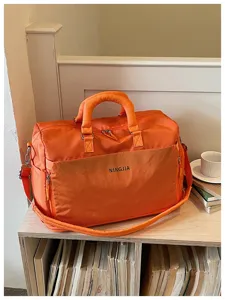 Orange travel duffel bag detail showcasing large capacity, sturdy handles and front pocket design.