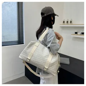 Detail view of white quilted travel duffel bag, showing durable shoulder strap and large capacity.