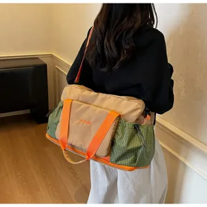 Detail view of a large travel duffel bag with orange handles and green plaid side pockets.