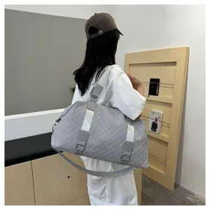 Detailed view of a grey quilted travel gym bag worn by a model in a clean indoor room setting.