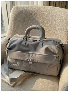 Quilted travel duffle bag in soft grey with top handles and strap for gym and trips.