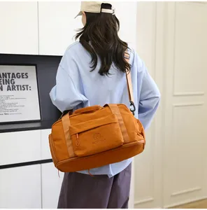 Detail view of orange travel duffel bag with shoulder strap and front pocket in indoor setting.