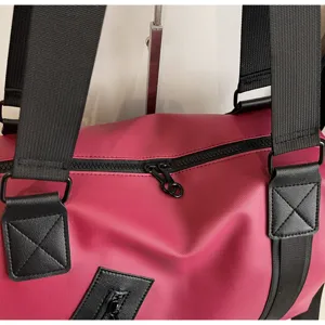 Gros plan d'un sac de voyage rouge montrant des sangles noires durables et des zips métalliques.