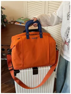 Detailed view of the orange travel duffel bag showing front branding and durable dual handles.