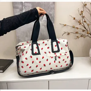 Detailansicht der weißen Kord Reisetasche mit rotem Erdbeerprint und schwarzen Trägern.