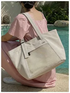 Detail view of beige canvas tote bag with front mesh pocket and stylish letter print.