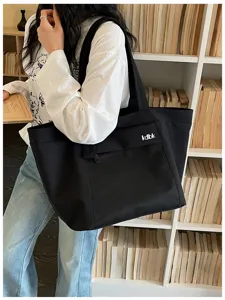 Black canvas tote bag with front mesh pocket and letter print, ideal for daily commute and travel.
