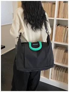 Detail view of large capacity black travel duffel bag with green handle and shoulder strap.