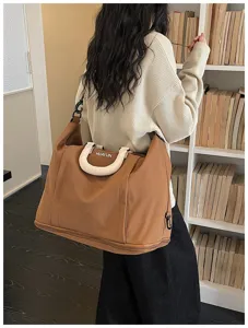 Detail view of the brown travel duffel bag showing white handle and expandable bottom.