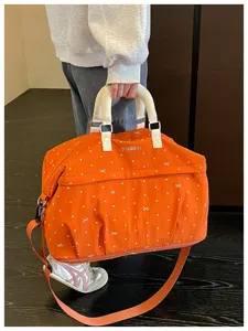 Detailed shot of orange travel duffel bag with white dots, bow embroidery, and handles.