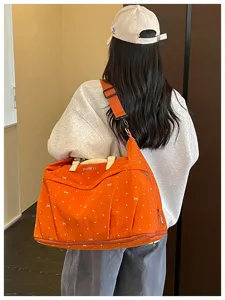 Detail shot of the orange travel duffel bag with bow pattern, showing shoulder strap and zipper.