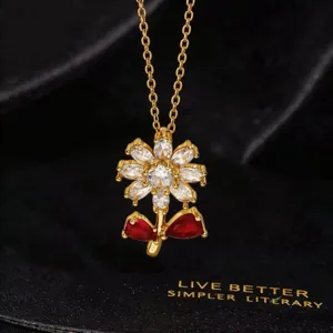 Detalle del collar con colgante de girasol brillante, circonitas y hojas rojas.