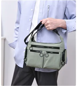 Detail shot of the light green multi-pocket casual crossbody bag with black zippers.