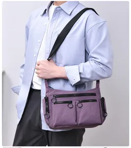 Detail shot of a purple multi-pocket crossbody bag with ring zipper pulls and nylon fabric.