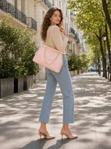 Detail view of pink kisslock handbag styled with pearl chain strap in outdoor street scene.