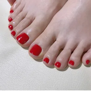 Detailopname van glanzende rode neppe teennagels, ideaal voor een snelle zomerpedicure.