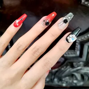 Detalle de primer plano de uñas postizas largas con rosas negras rojas y pedrería brillante.