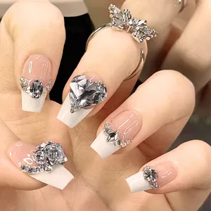 Primer plano detallado de uñas postizas de lujo con puntas blancas francesas y diamantes brillantes.